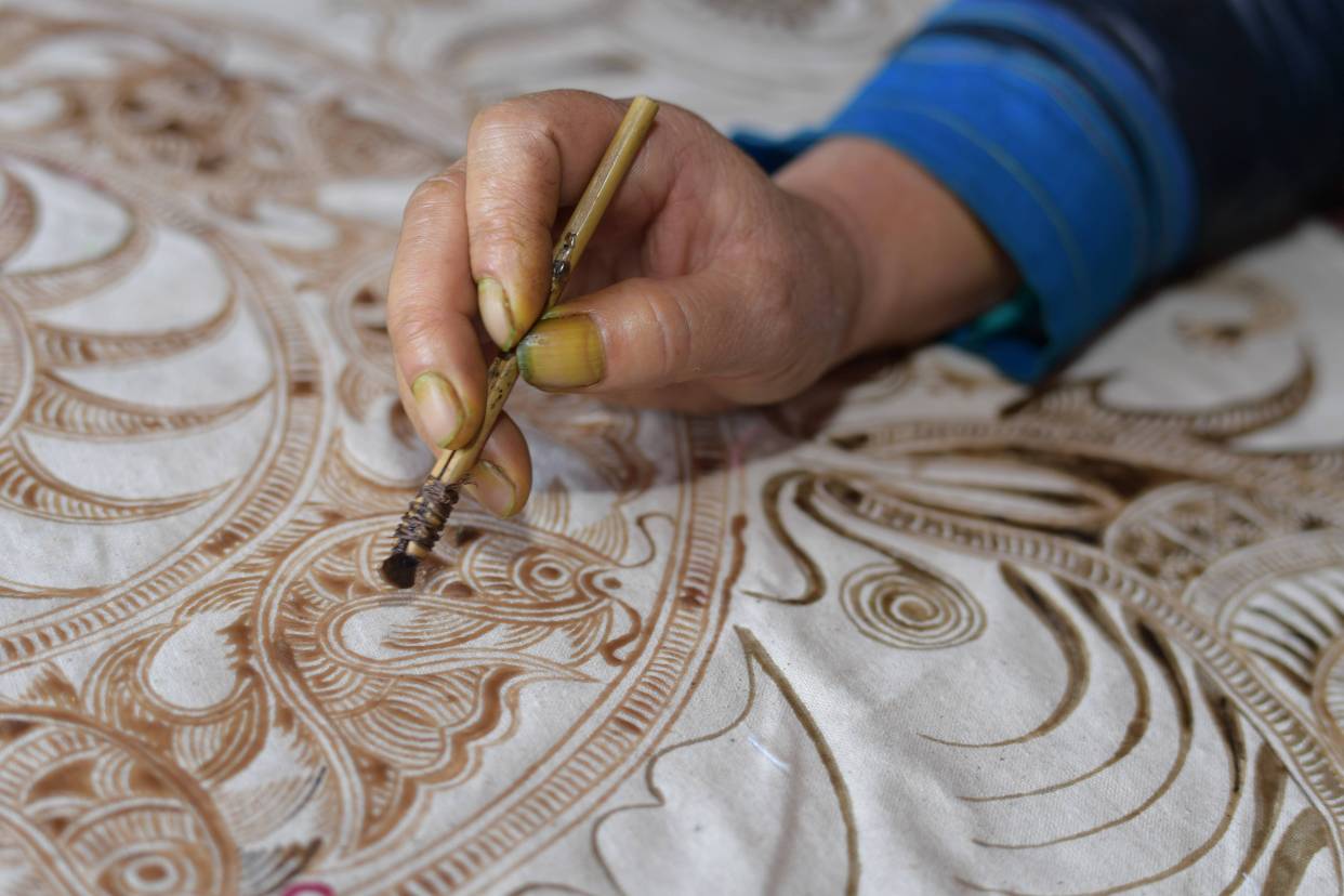 Artisan drawing intricate Miao batik pattern by hand using a wax knife